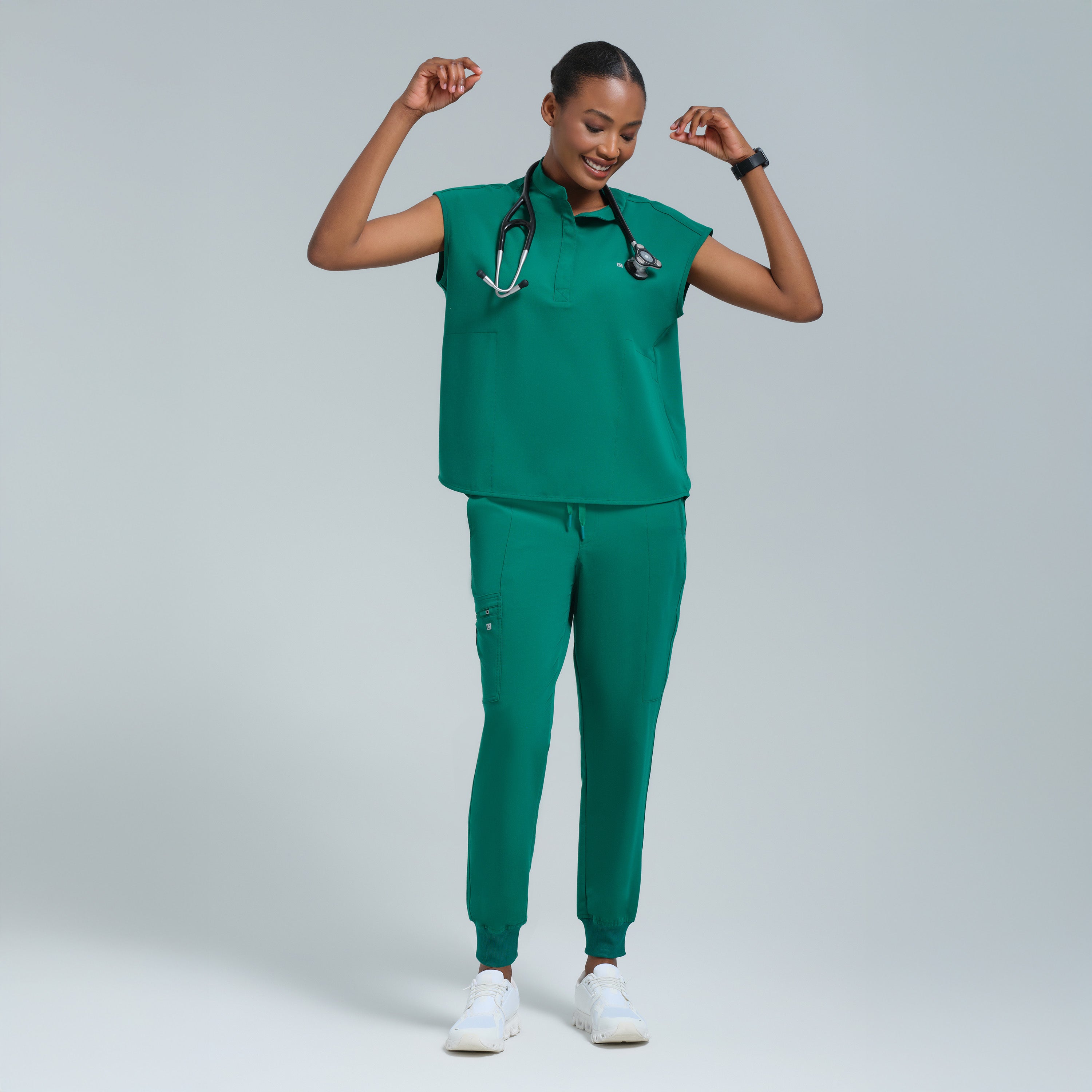 Person wearing a green medical scrub set with white sneakers on a light gray background