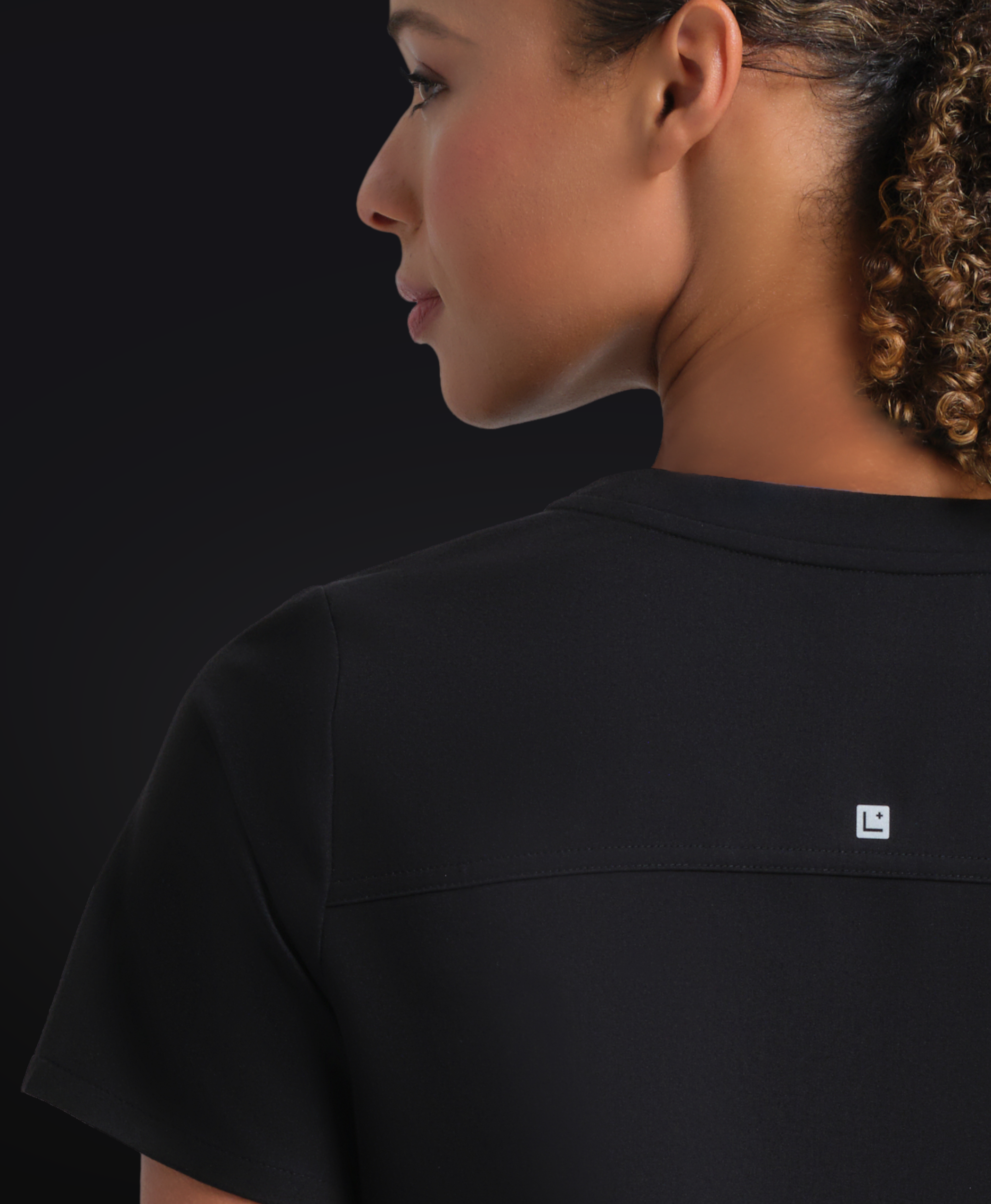 Person wearing a black shirt with a small logo on a dark background