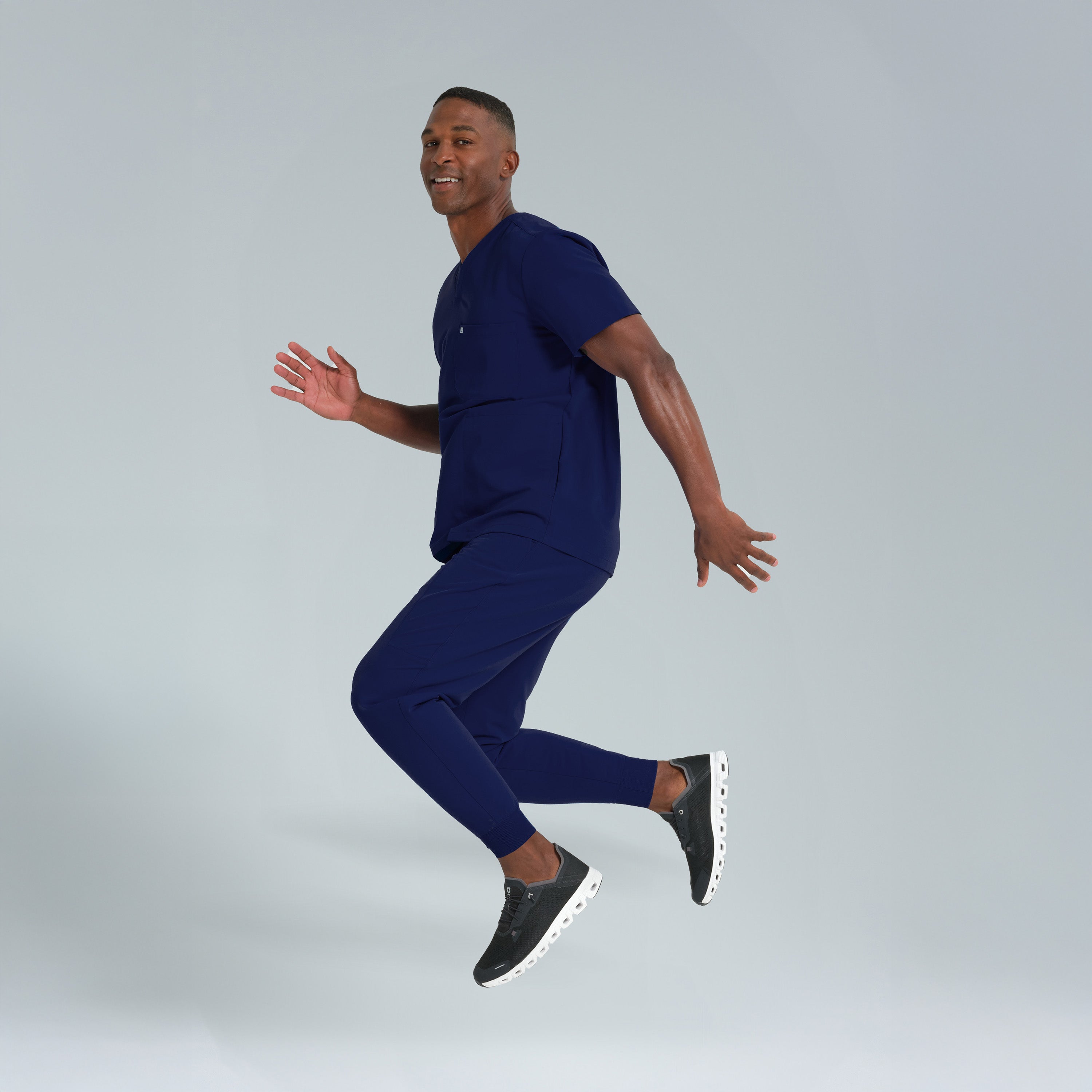 Man in a navy blue outfit jumping against a gray background