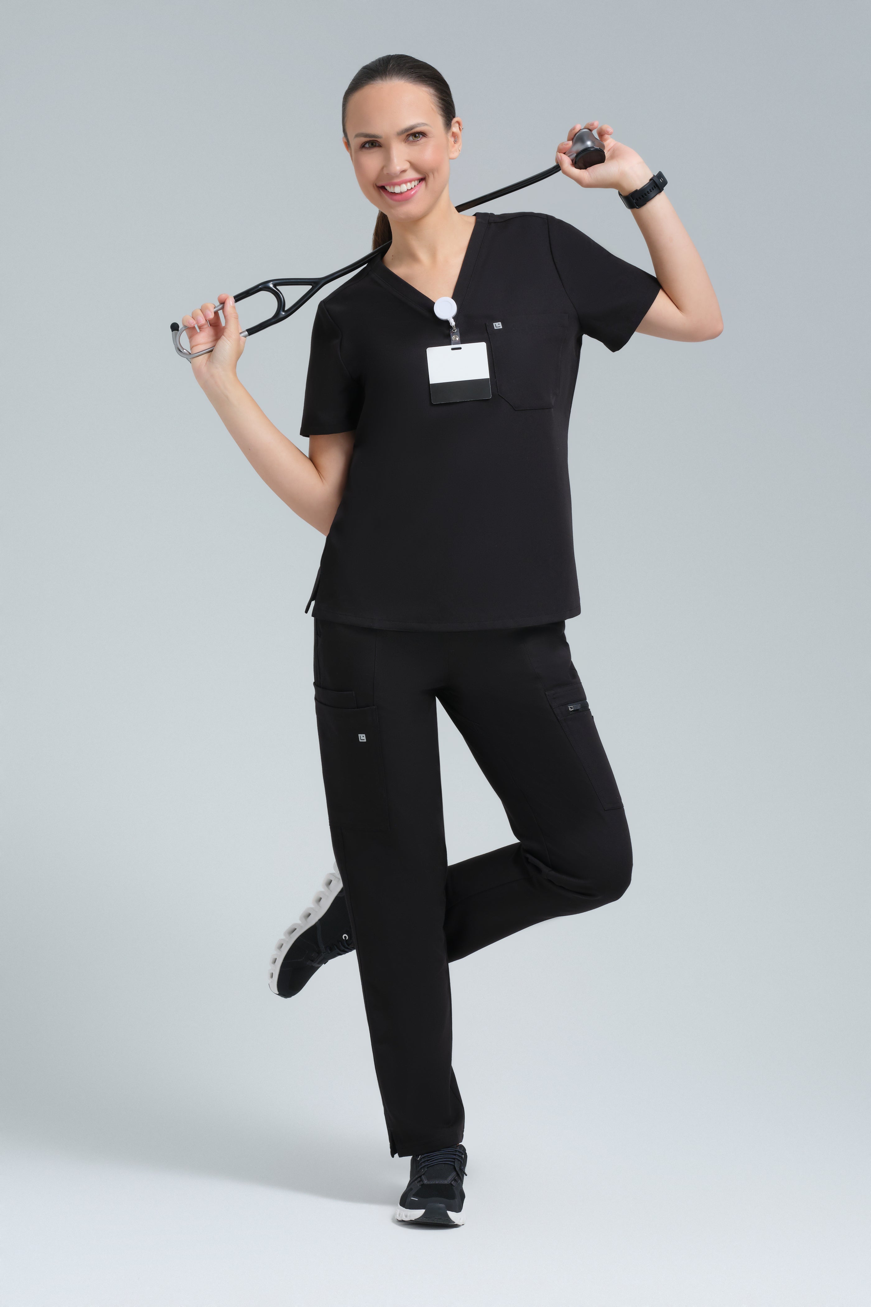 Woman in black medical scrubs holding a stethoscope on a gray background