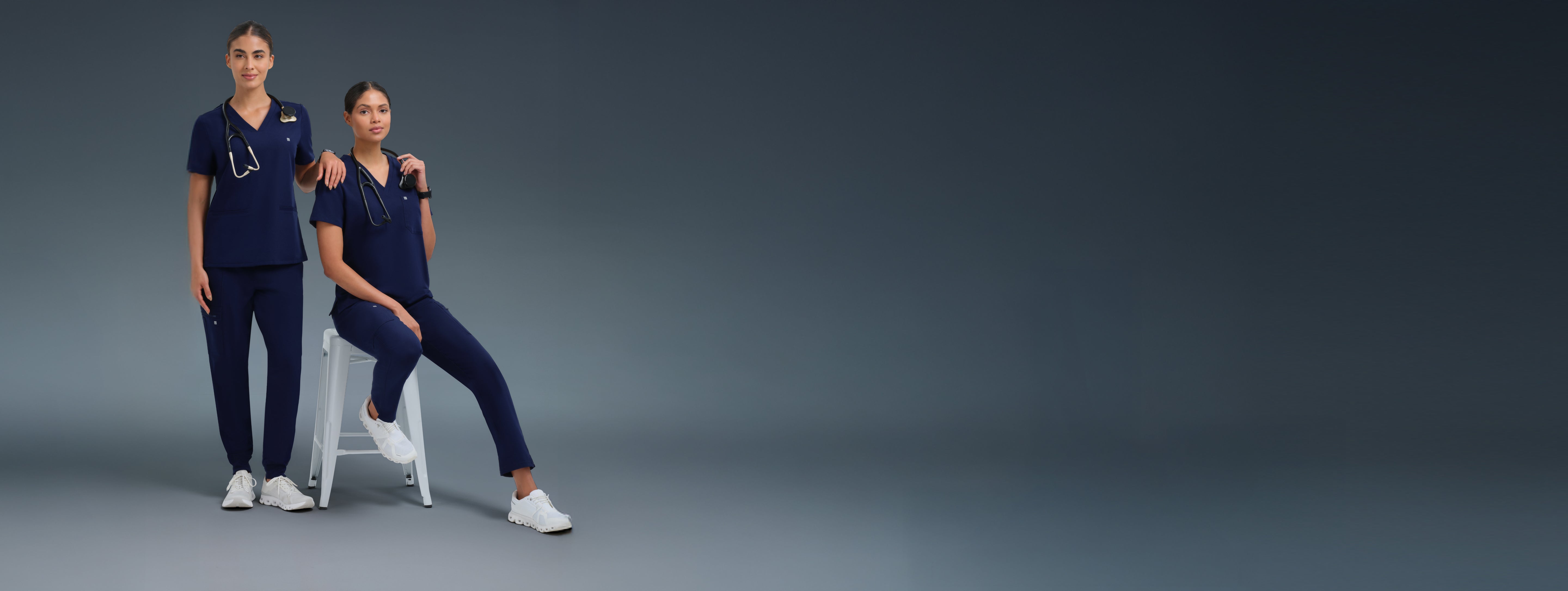 Two individuals in matching navy blue scrubs standing against a dark gray background