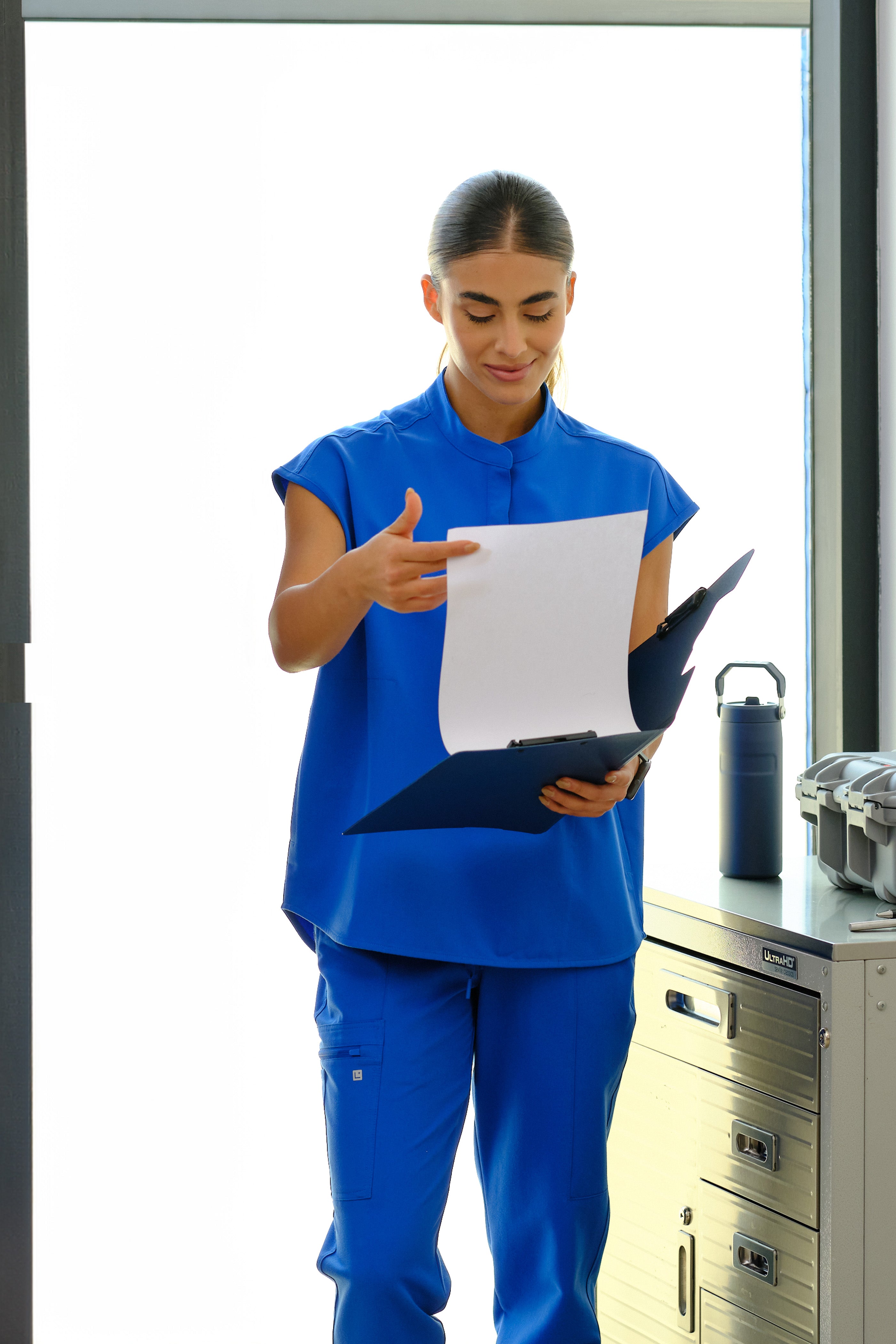 Person in blue uniform holding a document in a clinical setting