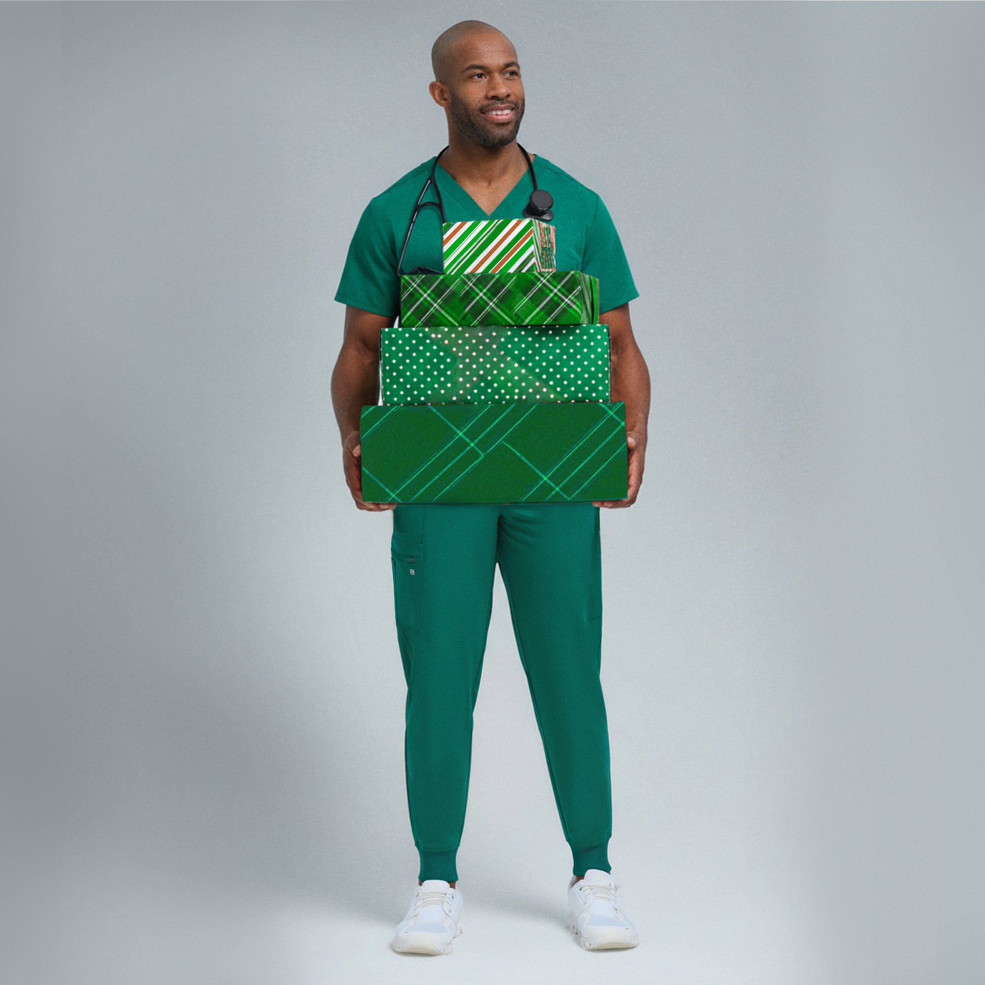 Man in green scrubs holding green gift boxes against a gray background
