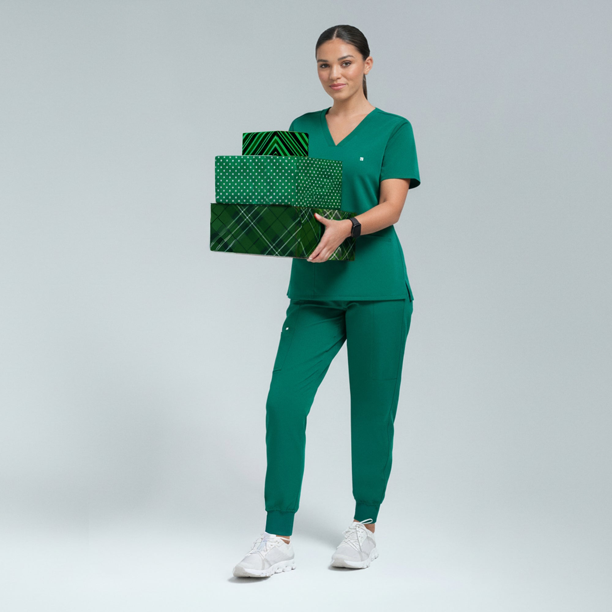 Person wearing green scrubs holding green gift boxes on a light gray background