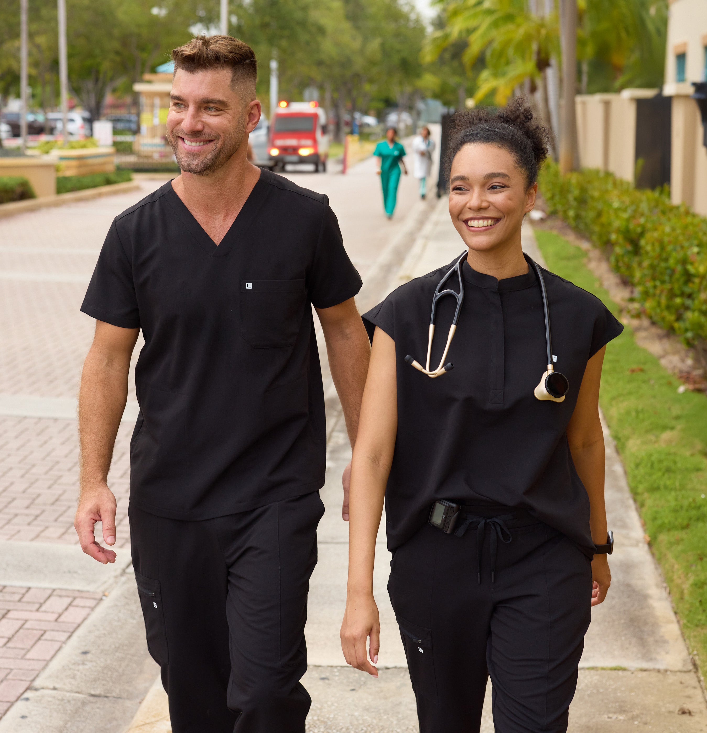 Two healthcare professionals in black scrubs walking outdoors on a sidewalk.